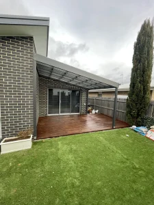 Covered timber deck beside artificial turf and a brick home