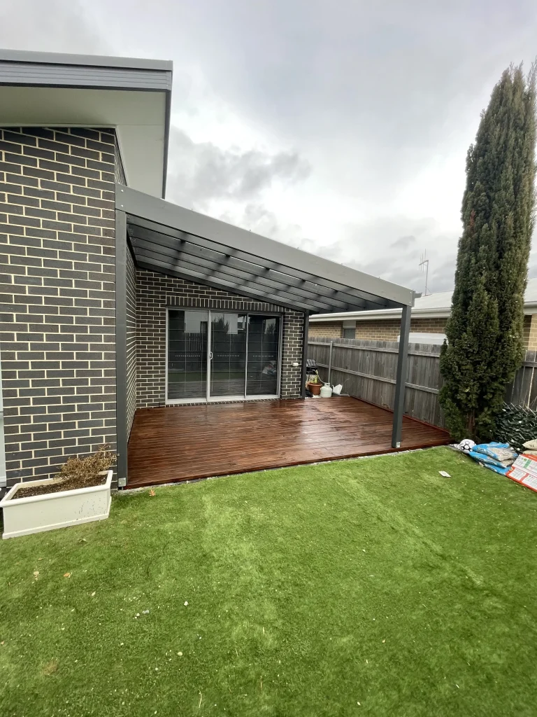 Covered timber deck beside artificial turf and a brick home
